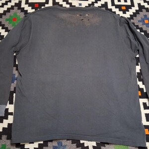 Puede incluir: Una camiseta de manga larga gris carb&oacute;n con detalles desgastados. La camiseta tiene cuello redondo y pu&ntilde;os en un gris m&aacute;s claro. La parte trasera de la camiseta tiene varios agujeros peque&ntilde;os cerca del cuello, d&aacute;ndole un aspecto usado.