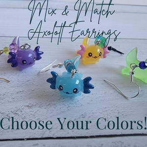 May include: Axolotl earrings in purple, yellow, blue, and green. Each earring features a small axolotl charm with beaded accents. The text "Mix & Match Axolotl Earrings" and "Choose Your Colors!" are displayed.
