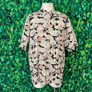 May include: Button-down short-sleeve shirt with a black, white, gray, and pink floral pattern. The shirt is displayed on a white mannequin. The shirt has a collared neckline and button closures.