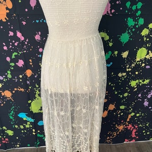 Pu&ograve; includere: Un abito senza spalline color crema con ricami floreali intricati. L'abito presenta un corpetto aderente e una gonna fluida e trasparente che arriva a met&agrave; polpaccio, rifinita con un orlo con frange. Il tessuto &egrave; delicato e leggero.