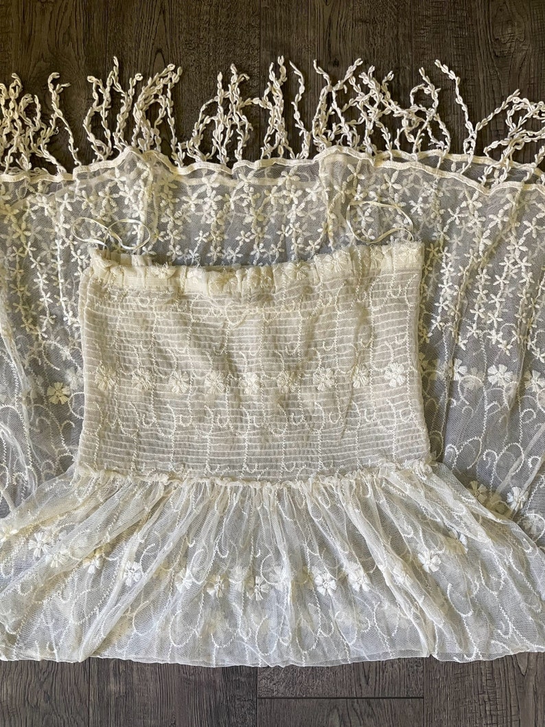 Pu&ograve; includere: Abito in pizzo color crema con ricami floreali. L'abito presenta uno scollo a balze, un corpetto aderente e una gonna svasata. La parte superiore dell'abito presenta linee orizzontali. L'abito &egrave; realizzato in un tessuto delicato e trasparente.