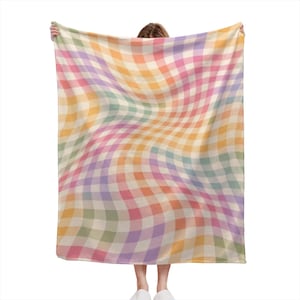 May include: A rectangular throw blanket featuring a distorted, wavy gingham check pattern in a soft pastel color palette of light pink, yellow, lavender, and mint green. The fabric displays a repeating grid design that appears to ripple across the surface.