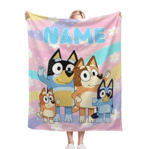 May include: A rectangular fleece blanket featuring a pastel rainbow wavy background with white daisy flowers and sparkles. The center displays four cartoon dog characters in blue and orange. The word NAME is printed in large light blue letters at the top.