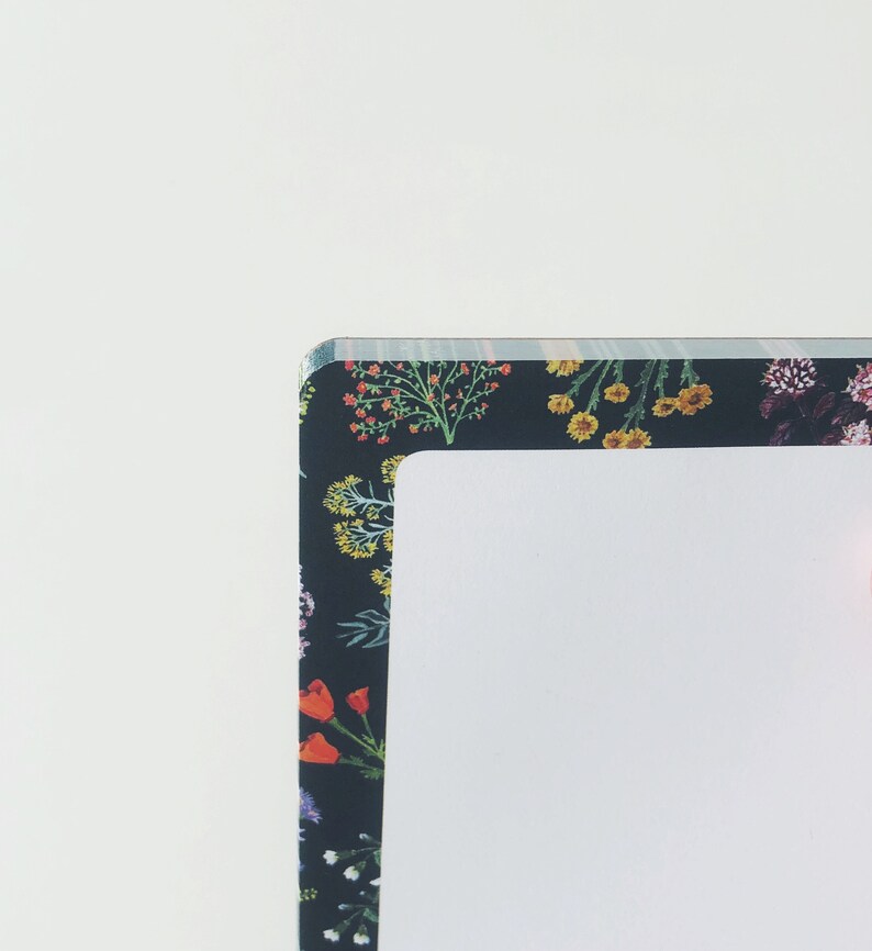 May include: A notebook with a floral pattern border. The border features a dark background with colorful flowers in shades of red, yellow, and purple. The notebook has a white interior.