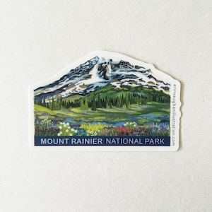 May include: A sticker featuring a watercolor illustration of Mount Rainier National Park. The image shows a snow-capped mountain, green trees, and colorful wildflowers. The text "MOUNT RAINIER NATIONAL PARK" is displayed on a navy blue banner.