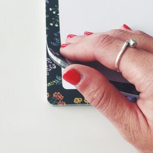 May include: A black floral patterned notebook with a white interior is being opened. The notebook's cover features a dark background with colorful flowers. A silver ring with a small blue stone is on a finger.