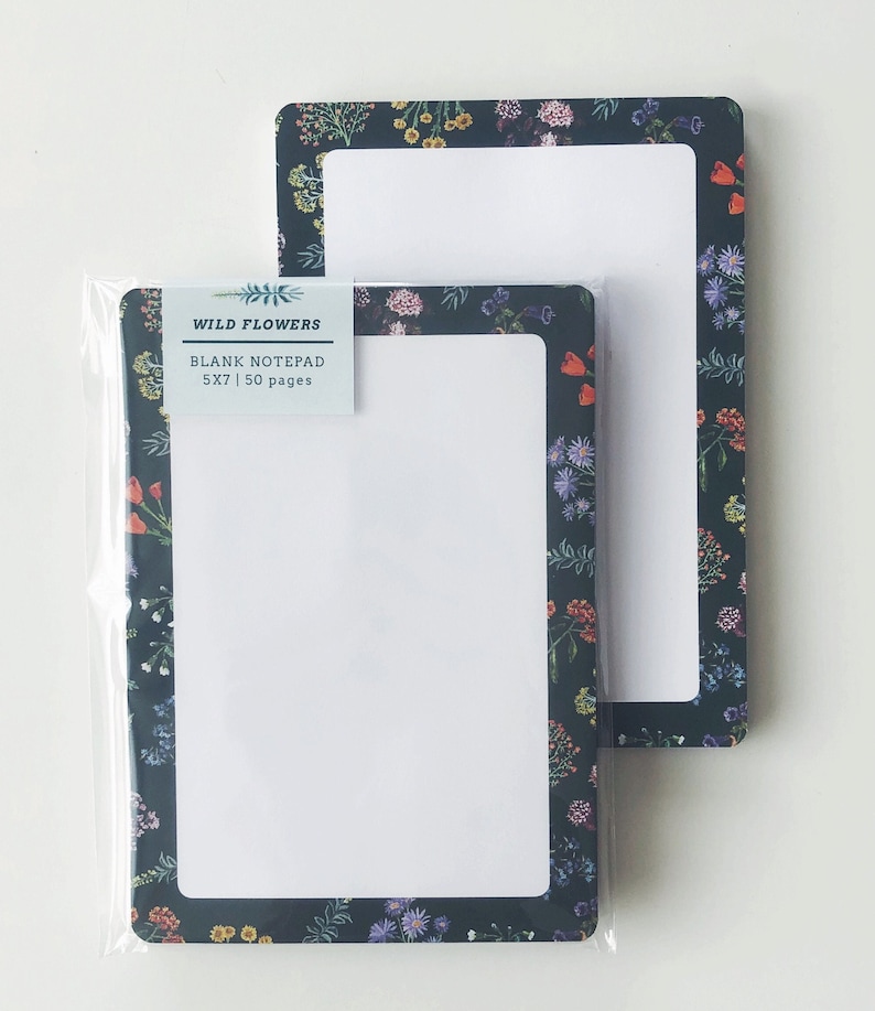 May include: Two rectangular blank notepads with a floral design border. The notepads are 5x7 inches and have a dark background with colorful flowers. One notepad is in a clear plastic sleeve. The label reads "Wild Flowers Blank Notepad 5x7 | 50 pages."