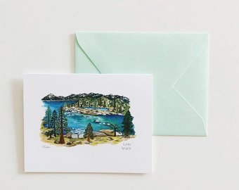 May include: A watercolor illustration of Lake Tahoe on a white card, with a matching light green envelope. The artwork depicts a blue lake surrounded by trees and mountains, with the words "Lake Tahoe" printed on the card.