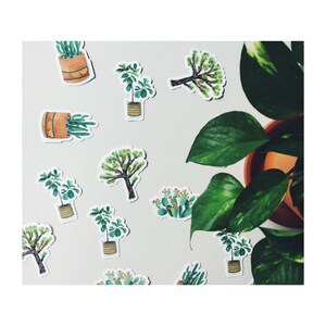 May include: A collection of plant-themed stickers featuring watercolor illustrations of cacti, trees, and potted plants. The stickers are in various shapes and sizes, with a neutral background and a potted plant in the corner.