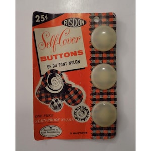 Puede incluir: Paquete vintage de botones Risdon Self-Cover de nailon Du Pont. El paquete es naranja con detalles de cuadros blancos y negros y presenta tres botones transparentes en forma de cúpula. El texto del paquete incluye "Self-Cover Buttons" y "Stain-Proof Nylon".