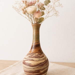 May include: A ceramic vase with a marbled pattern of brown and cream swirls, featuring a narrow neck and a rounded base. The vase is filled with a bouquet of dried flowers, including white and pink blossoms and green eucalyptus leaves.
