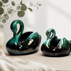 May include: Two ceramic swan-shaped planters featuring a glossy, deep emerald green and black glaze. The swan figures are sculpted with curved necks and detailed wing textures, designed as open vessels for small plants or decorative items.