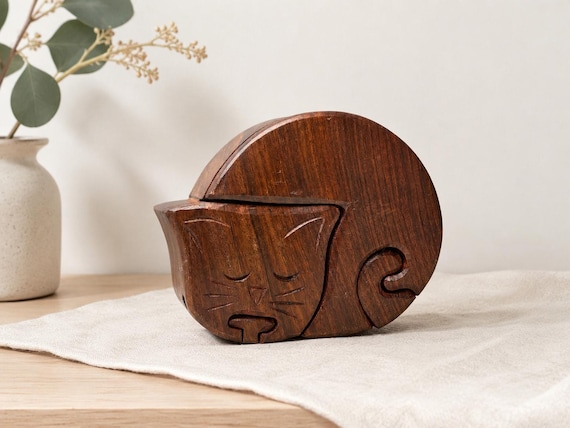 A hand-carved wooden cat that secretly unlocks — a tactile brain teaser and hidden compartment box in one charming sculptural object.