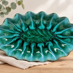 May include: An oval ceramic bowl with a scalloped, ruffled edge. The bowl features a glossy glaze that transitions from a deep, dark forest green in the centre to a vibrant, lighter turquoise blue along the outer, wavy rim of the dish.
