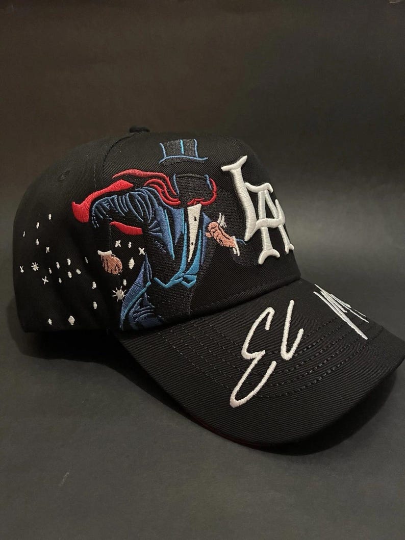 K&ouml;nnte beinhalten: Schwarze Baseballkappe mit gesticktem Zauberer-Motiv in Rot, Blau und Wei&szlig;. Die Kappe zeigt die Buchstaben "LA" in Wei&szlig; und die Zahl "13" in wei&szlig;er Schrift auf dem Schirm. Klassisches Sechs-Panel-Design.