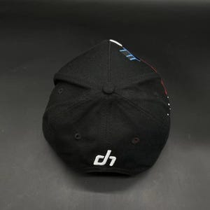 K&ouml;nnte beinhalten: Schwarze Baseballkappe mit gebogenem Schirm. Die Kappe hat ein wei&szlig;es Logo an der Seite und ein Design in Blau, Wei&szlig; und Rot auf der Oberseite. Die Kappe ist aus einem strukturierten Stoff.