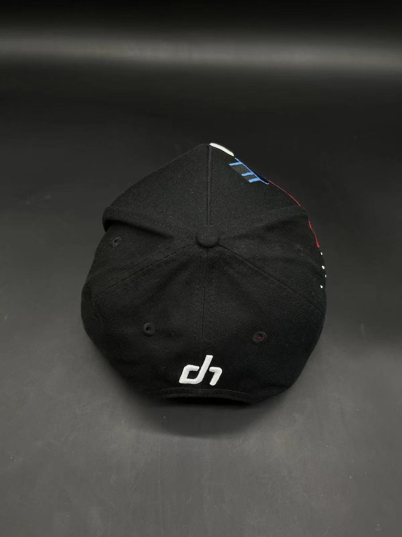 K&ouml;nnte beinhalten: Schwarze Baseballkappe mit gebogenem Schirm. Die Kappe hat ein wei&szlig;es Logo an der Seite und ein Design in Blau, Wei&szlig; und Rot auf der Oberseite. Die Kappe ist aus einem strukturierten Stoff.