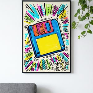 May include: A framed art print depicting a hand-drawn floppy disk illustration. The artwork uses bright colours such as blue, yellow, pink, and green, in a retro 80s style. The background features abstract shapes and lines, reminiscent of the era.