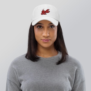 May include: White baseball cap with a red and black lobster embroidered on the front. The cap has a curved brim and an adjustable strap at the back. A casual accessory for everyday wear.