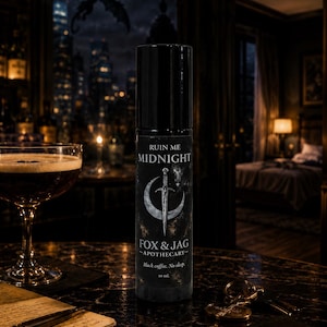 May include: A black cylindrical bottle labeled Ruin Me Midnight by Fox & Jag Apothecary. The label features a silver crescent moon and sword graphic with the text Black coffee. No sleep. and 10 ml. The bottle has a black cap and stands upright.