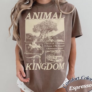 May include: Espresso-colored t-shirt with "ANIMAL KINGDOM" printed in white. The design includes illustrations of the Tree of Life, Expedition Everest, The Boneyard, and Kilimanjaro Safaris. The shirt is from Comfort Colors.
