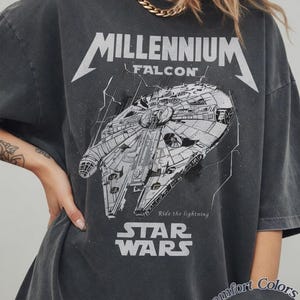Peut inclure: T-shirt gris foncé avec un dessin du vaisseau spatial Faucon Millenium, le texte "Millennium Falcon" et "Star Wars". Le t-shirt porte également l'inscription "Ride the lightning".