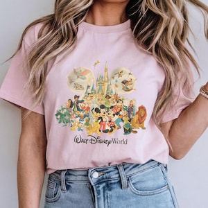 May include: Pink t-shirt featuring a colorful graphic of Disney characters, including Mickey Mouse, Minnie Mouse, and Simba, in front of a castle. The words "Walt Disney World" are printed below the graphic.