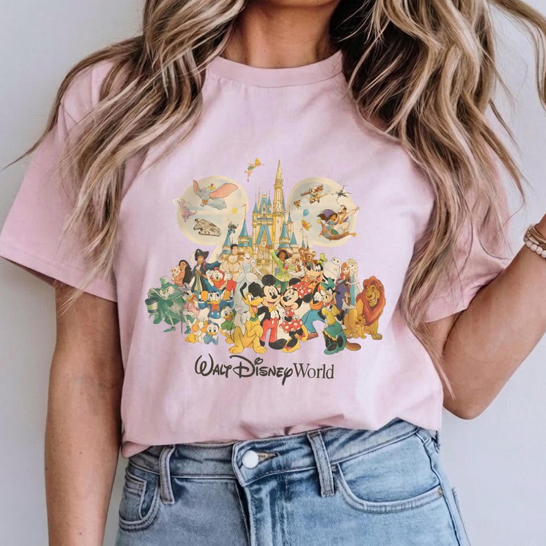 May include: Pink t-shirt featuring a colorful graphic of Disney characters, including Mickey Mouse, Minnie Mouse, and Simba, in front of a castle. The words "Walt Disney World" are printed below the graphic.