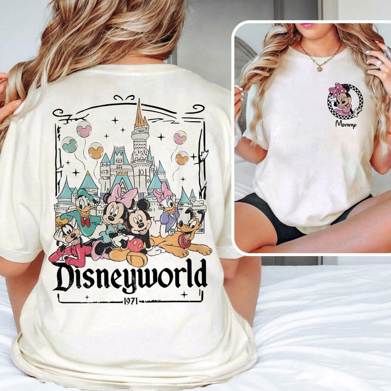May include: Cream-colored t-shirt featuring a Disneyworld graphic on the back with Mickey, Minnie, Donald, Daisy, Goofy, and Pluto. The front of the shirt has a Minnie Mouse graphic with the word "Mommy".