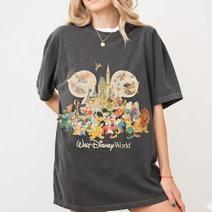 May include: Dark gray t-shirt featuring a colorful graphic of Disney characters, including Mickey Mouse, Donald Duck, and Simba, in front of a castle. The text "Walt Disney World" is printed below the graphic. The shirt has short sleeves.