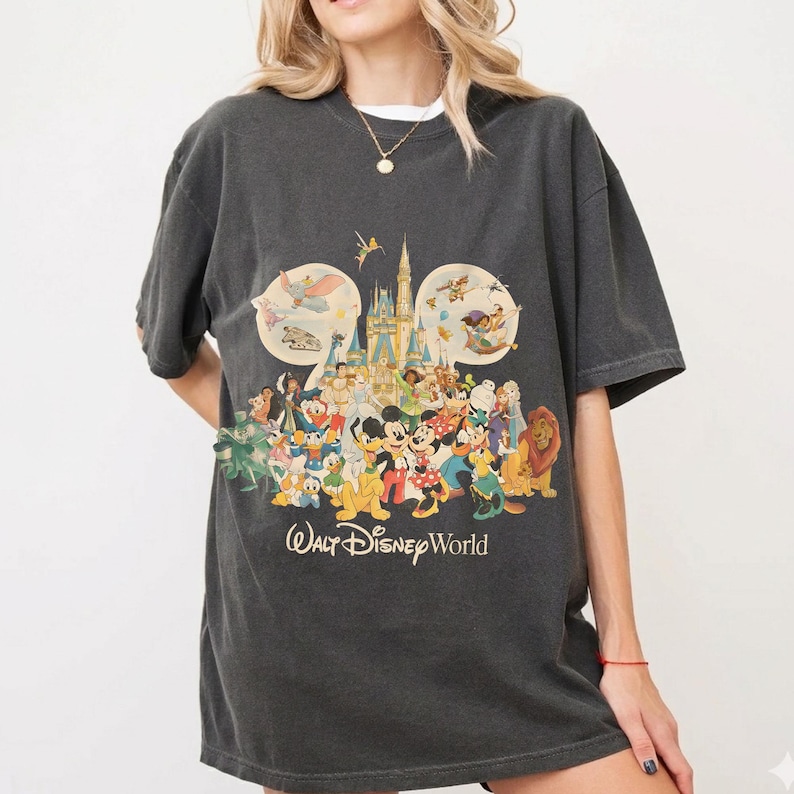May include: Dark gray t-shirt featuring a colorful graphic of Disney characters, including Mickey Mouse, Donald Duck, and Simba, in front of a castle. The text "Walt Disney World" is printed below the graphic. The shirt has short sleeves.