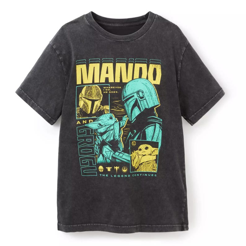 K&ouml;nnte beinhalten: Dunkelgraues T-Shirt mit einer Grafik von Mando und Grogu aus The Mandalorian. Das Design enth&auml;lt den Text "MANDO" in Gelb und "GROGU" in T&uuml;rkis. Der Satz "THE LEGEND CONTINUES" ist ebenfalls vorhanden.