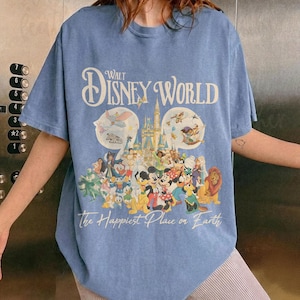 May include: Blue short-sleeved t-shirt featuring a Walt Disney World graphic. The design includes the park's logo, a castle, and various Disney characters. The text "The Happiest Place on Earth" is printed below the characters.