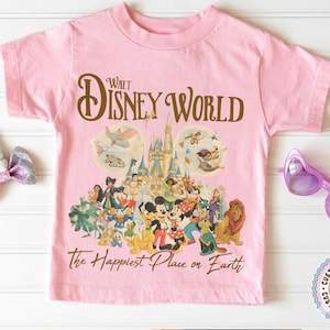 May include: Pink t-shirt featuring a colorful graphic of Disney characters and the text "Walt Disney World" in brown script. The shirt also includes the phrase "The Happiest Place on Earth" in a script font.