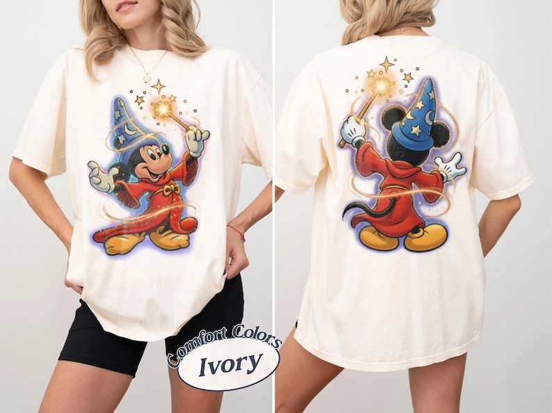 May include: An ivory t-shirt featuring a graphic of a cartoon mouse dressed as a wizard in a red robe and blue star-patterned hat. The front shows the mouse facing forward holding a glowing wand, while the back shows the mouse from behind.