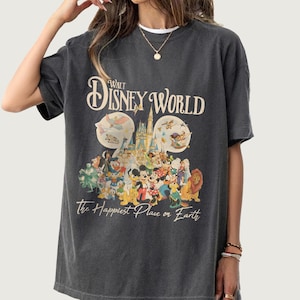 May include: Dark gray t-shirt featuring the text "Walt Disney World" above a colorful graphic of Disney characters and the phrase "The Happiest Place on Earth". The design includes Mickey Mouse, Minnie Mouse, and other beloved characters.