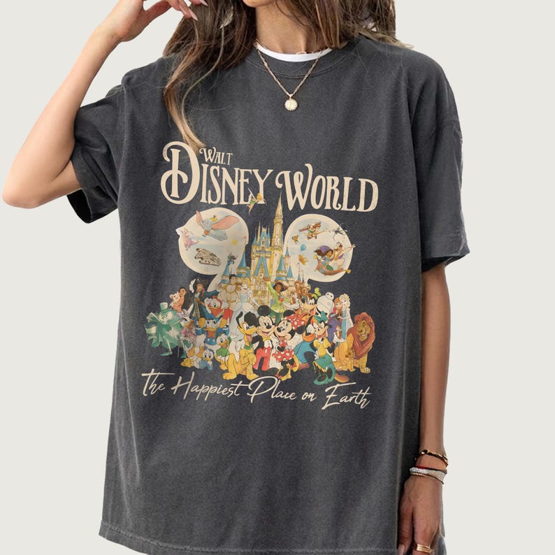 May include: Dark gray t-shirt featuring the text "Walt Disney World" above a colorful graphic of Disney characters and the phrase "The Happiest Place on Earth". The design includes Mickey Mouse, Minnie Mouse, and other beloved characters.