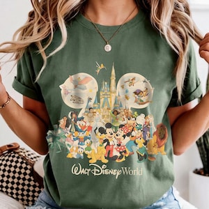 May include: Green t-shirt featuring a colorful graphic of various Disney characters, including Mickey Mouse, Donald Duck, and Simba. The design includes the text "Walt Disney World" in a stylized font. The shirt has short sleeves.
