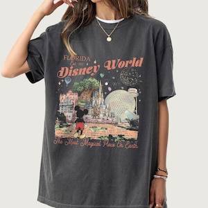 Puede incluir: Camiseta gris oscuro con un gr&aacute;fico colorido de los lugares emblem&aacute;ticos de Disney World, incluido el castillo de Cenicienta y Mickey Mouse. El texto dice "Florida Disney World" y "The Most Magical Place On Earth."