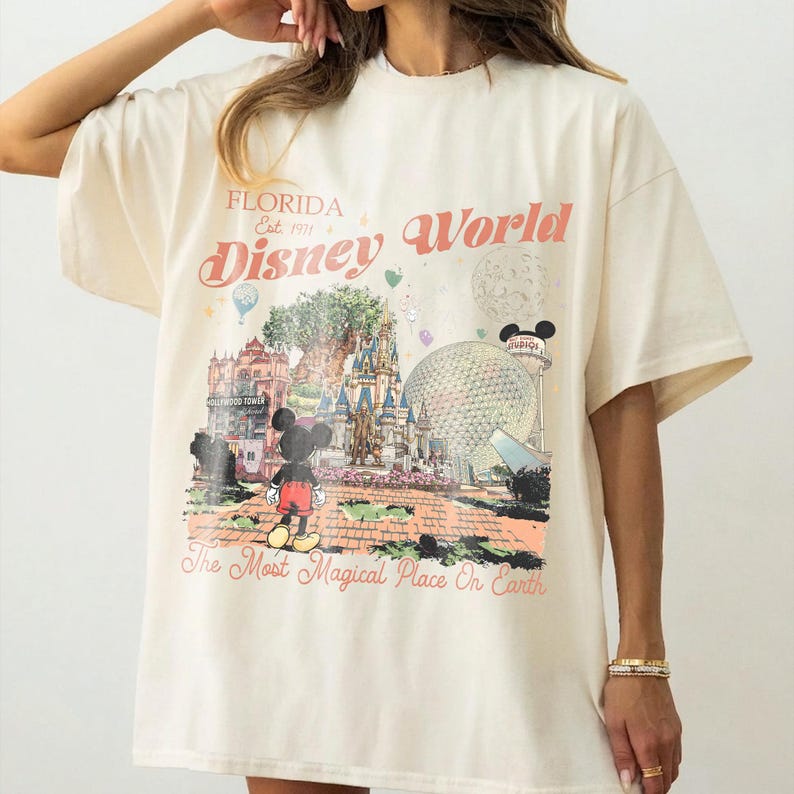 Puede incluir: Camiseta color crema con un dise&ntilde;o gr&aacute;fico de Disney World en Florida. El dise&ntilde;o incluye el texto "Florida Est. 1971 Disney World" y "The Most Magical Place On Earth", con Mickey Mouse, un castillo y una gran esfera.