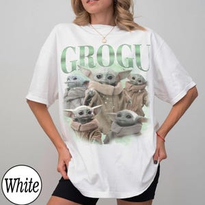 May include: White t-shirt featuring a graphic of Grogu, also known as Baby Yoda, from The Mandalorian. The word "GROGU" is printed in green above the image of Grogu. The t-shirt is a casual, oversized style.
