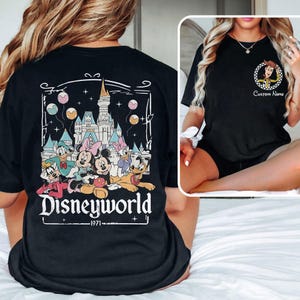 May include: Black t-shirt featuring a colorful graphic of Disney characters, including Mickey and Minnie Mouse, Donald and Daisy Duck, and Goofy, in front of a castle. The word "Disneyworld" is printed below the graphic, with "1971" underneath.