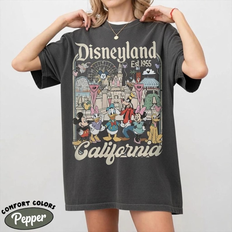 Peut inclure: T-shirt gris fonc&eacute; avec un motif Disneyland repr&eacute;sentant Mickey Mouse, Donald Duck et d'autres personnages. Le t-shirt porte l'inscription "Disneyland Est. 1955 California". C'est un t-shirt Comfort Colors Pepper.