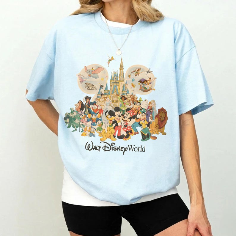 May include: Light blue t-shirt featuring a colorful graphic of Disney characters, including Mickey Mouse, Minnie Mouse, and others, in front of a castle. The words "Walt Disney World" are printed below the graphic.