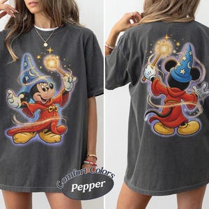May include: A charcoal gray t-shirt featuring a graphic of Mickey Mouse as a sorcerer. The front shows Mickey facing forward in a red robe and blue star-patterned hat holding a glowing wand. The back shows the same character from behind.