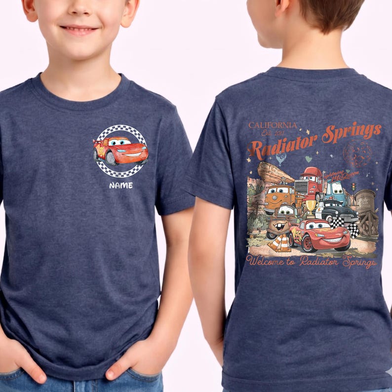 Puede incluir: Camiseta azul marino con un dise&ntilde;o de dibujos animados de Rayo McQueen de la pel&iacute;cula Cars. La parte delantera tiene una imagen circular con la palabra "NAME". La parte trasera presenta un gr&aacute;fico de Radiator Springs, California, con varios personajes de coches.