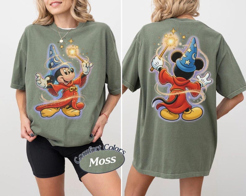 May include: A moss green t-shirt featuring a graphic of Mickey Mouse dressed as a wizard in a red robe and blue star-patterned hat, holding a glowing wand. The design appears on both the front and back of the shirt, with swirling light effects.