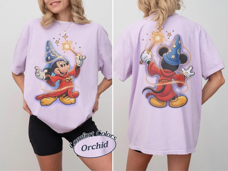 May include: An orchid-colored t-shirt featuring a graphic of Mickey Mouse as a sorcerer. The front shows Mickey facing forward with a wand, while the back shows Mickey from behind with a wand. The shirt has short sleeves and a crew neckline.
