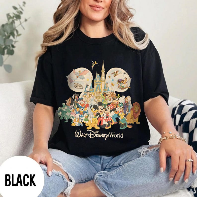 May include: Black t-shirt featuring a colorful graphic of Disney characters, including Mickey Mouse, Donald Duck, and others, with the text "Walt Disney World." The design includes a castle and the number 50. The word "BLACK" is in a white box.