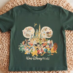 Puede incluir: Camiseta verde oscuro con un gr&aacute;fico colorido de personajes de Disney, incluyendo Mickey Mouse, Donald Duck y Simba, frente a un castillo. Las palabras "Walt Disney World" est&aacute;n impresas debajo de los personajes.